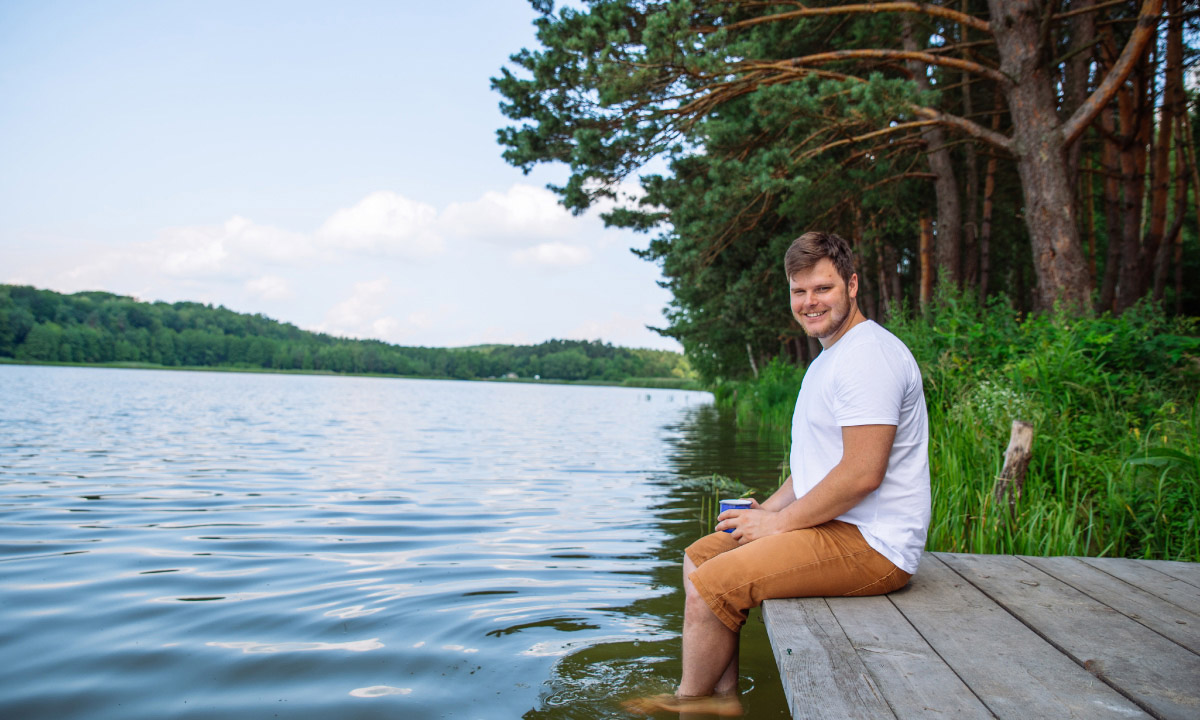 чоловік сидить на деревяному помості біля озера в лісі