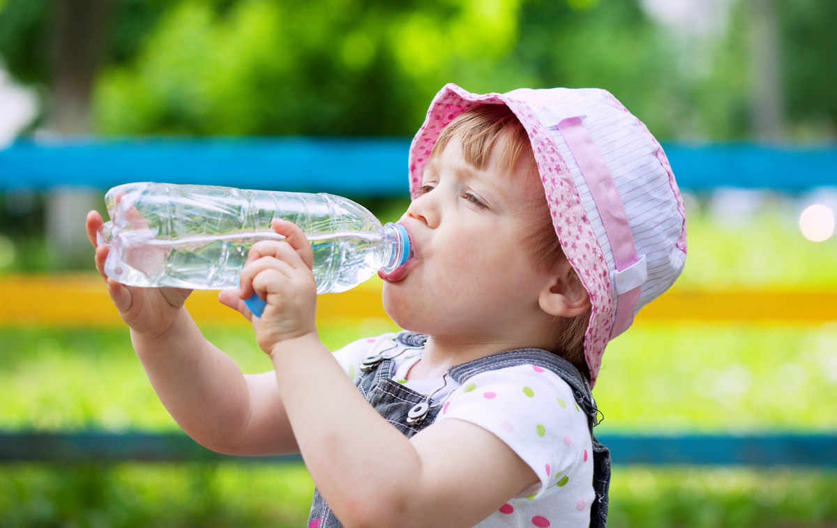 маленька дитинка на дитячому майданчику п'є воду із пластикової пляшки