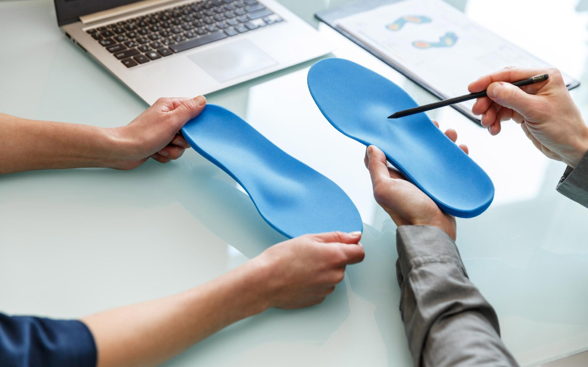 на зображенні прийом у лікаря, який на прикладі устілки показує та розповідає про правильне розміщення стопи