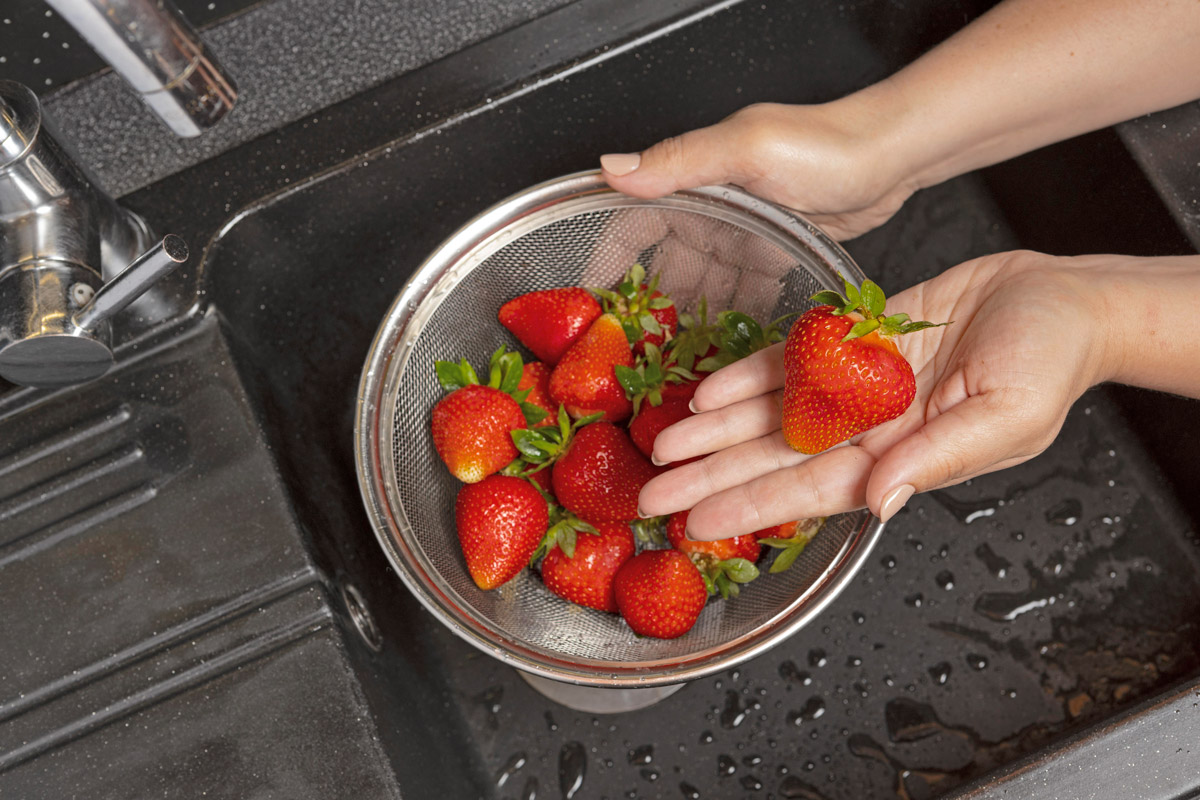 жінка миє полуницю у кухонній мийці