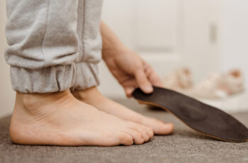 зображення стоп, де людина стоїть на рівній поверхні та намагається з'ясувати, чи є в неї плоскостопість, та тримає устілку в руці