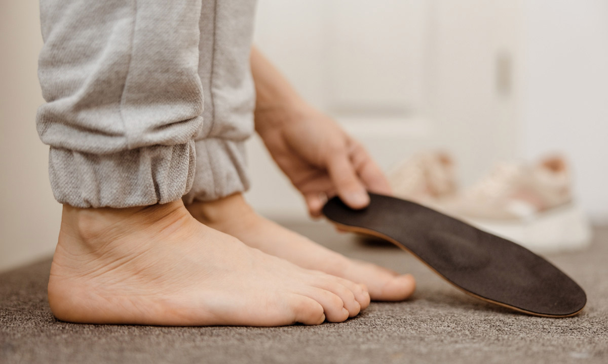 зображення стоп, де людина стоїть на рівній поверхні та намагається з'ясувати, чи є в неї плоскостопість, та тримає устілку в руці
