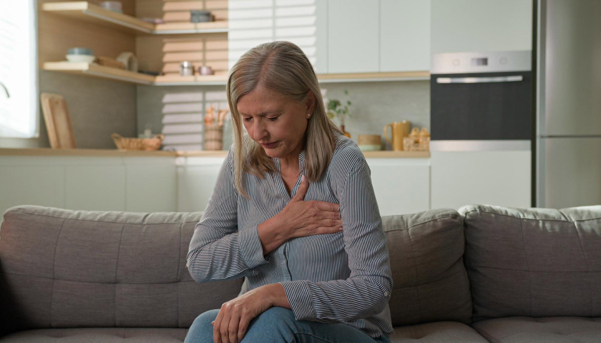 літня жінка сидить на дивані в себе вдома, та відчуваж сильний біль в ділянці грудини