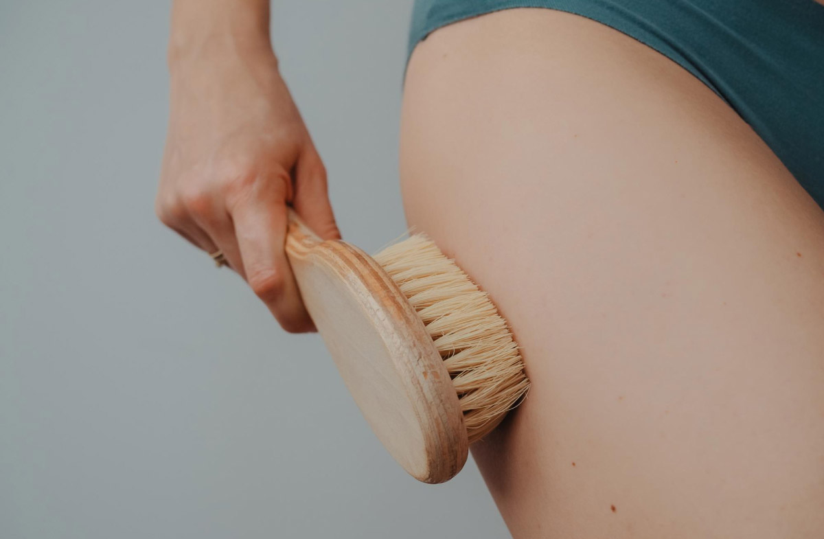 жінка масує шкіру стегон спеціальною щіткою для масажу