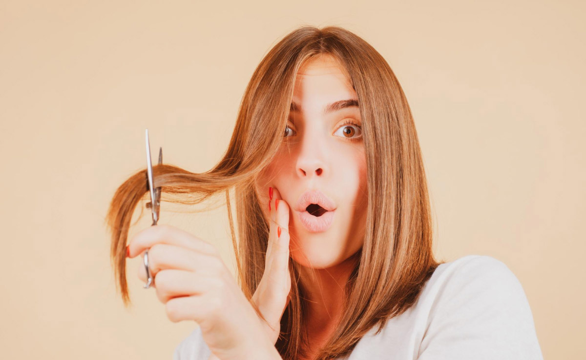 жінка тримає пасмо волосся в лезах ножиць ніби наважуючись його відрізати