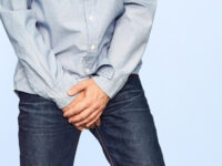 чоловік прикриває руками зону паху, тому що, певно, він відчуває біль та дискомфорт в цій зоні