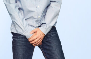 чоловік прикриває руками зону паху, тому що, певно, він відчуває біль та дискомфорт в цій зоні