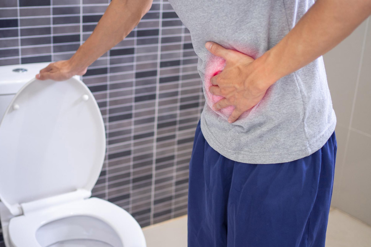 чоловік стоїть біля туалету та тримається за живіт через відчуття гострого болю