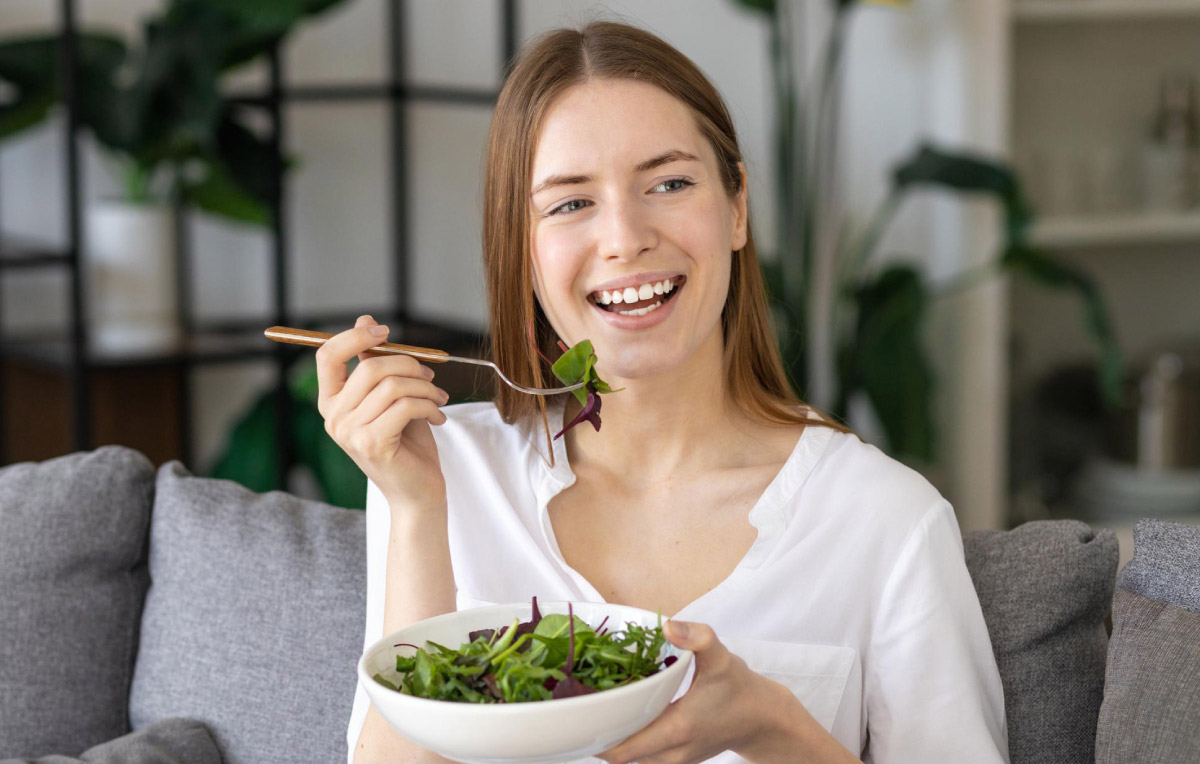 дівчина із радісним виглядом куштує зелений салат