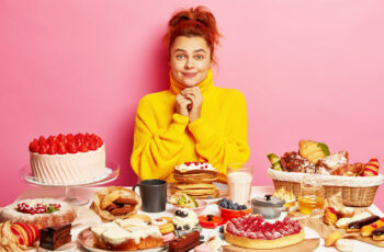 дівчинка сидить перед великим столом, який заповнений різноманіттям солодощів