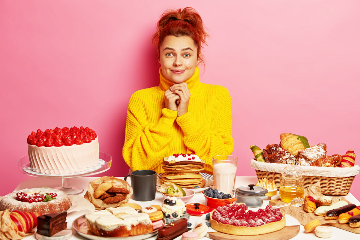 дівчинка сидить перед великим столом, який заповнений різноманіттям солодощів