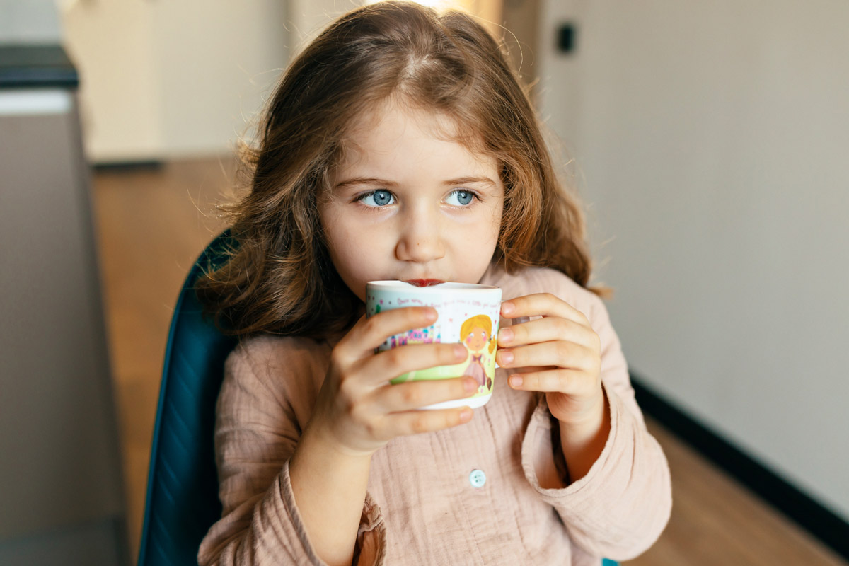 маленька сіроока дитина дівчинка п'є воду на кухні в себе вдома
