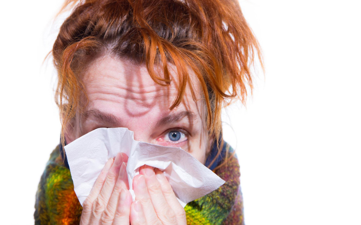 жінка прикривається хустинкою, що говорить про те, що її турбують симптоми алергії, як-то нежить та сльозоточивість