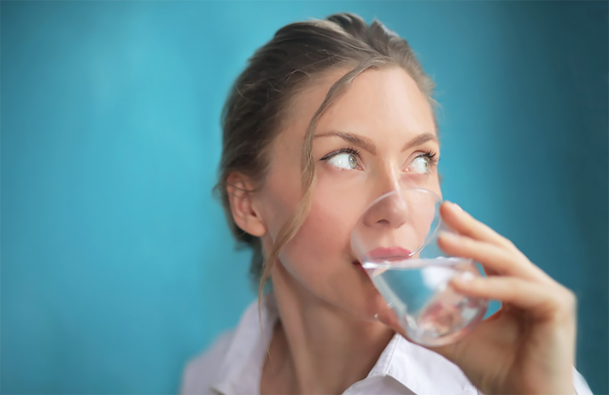 жінка п'є воду зі скляного прозорого стакана