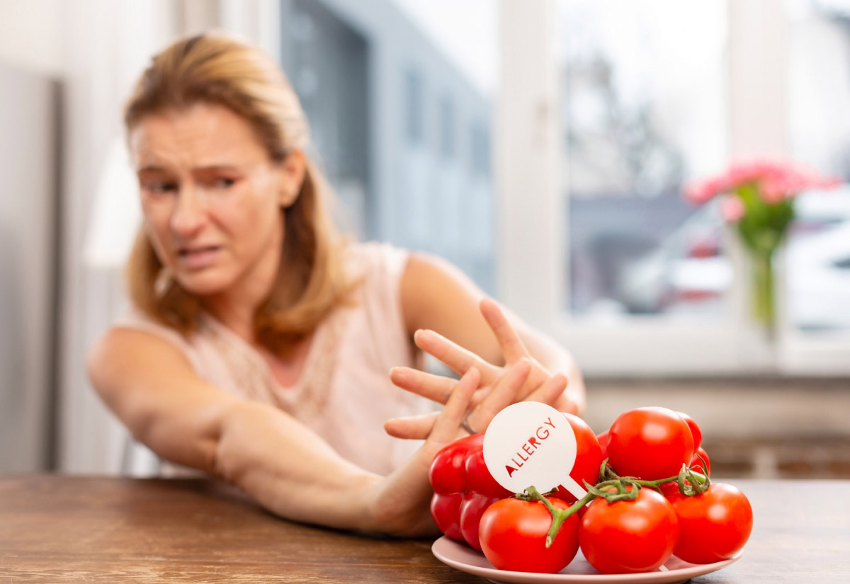 жінка витягнувши руки, відштовхує від себе помідори, адже, певно має на них алергію