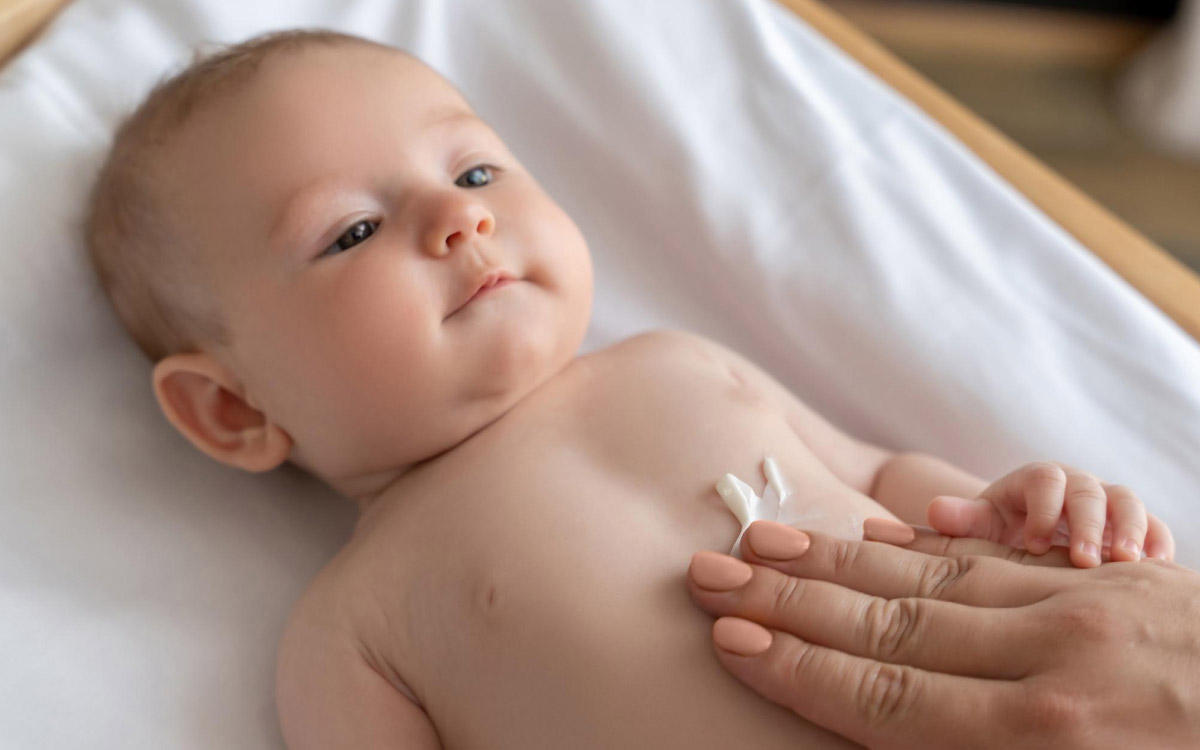 зображення материнської руки, яка мастить шкіру новонародженої дитини лосьйоном для заспокоєння шкірних покривів