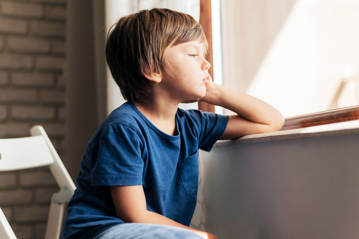 дитина сидить втомлена біля підвіконня