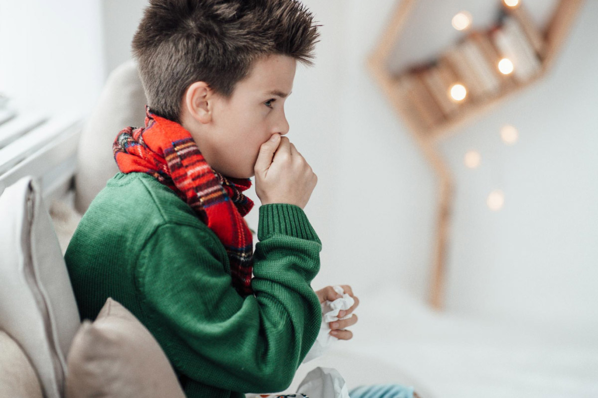 хлопчик сидить вдома закутаний із шарфом на шиї та страждає від застуди