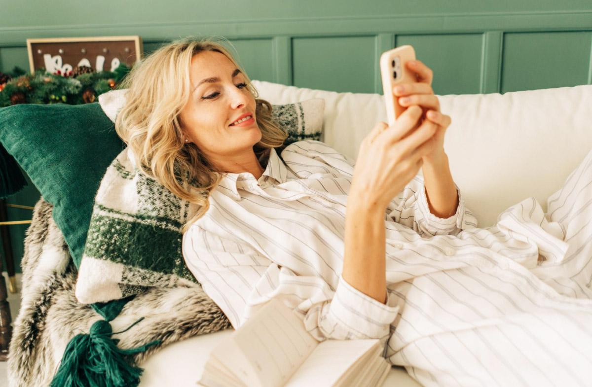 жінка лежить на дивані, відпочиває, та дивиться в телефон