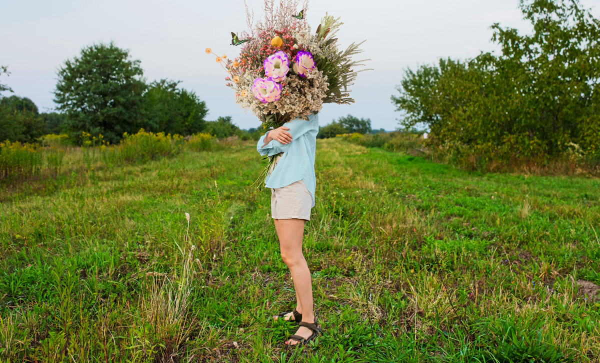 жінка тримає букет квітів, стоїть в полі