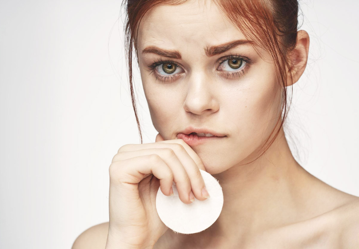 жінка виглядає стурбованою, тримає в руці ватний диск для зняття макіяжу