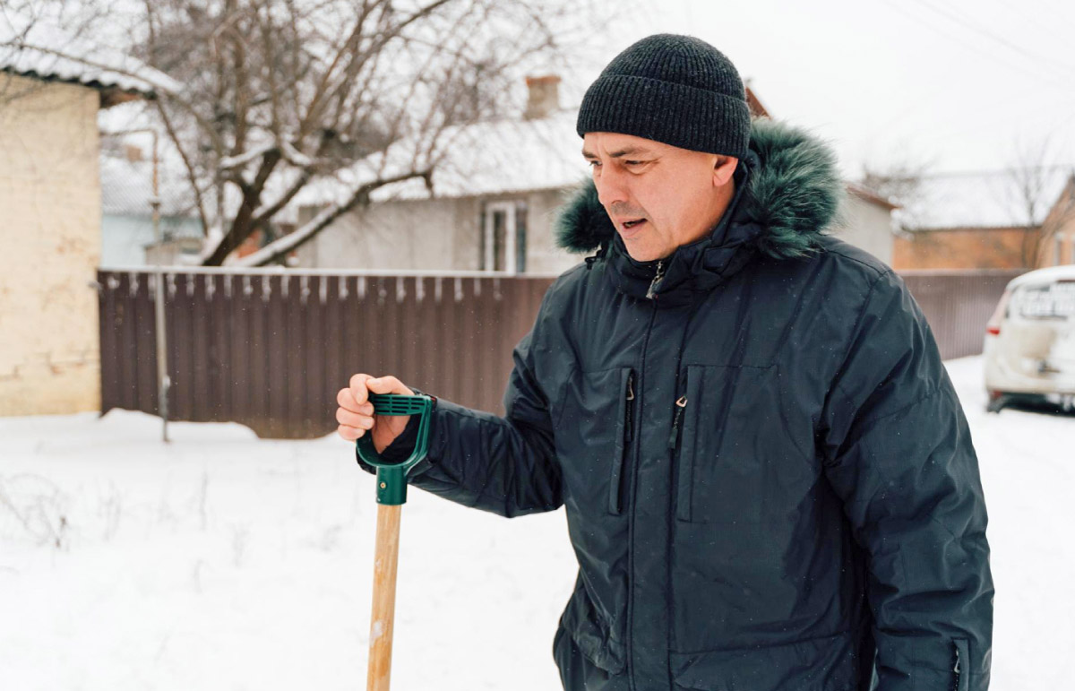 чоловік на подвір'ї розчищає сніг лопатою