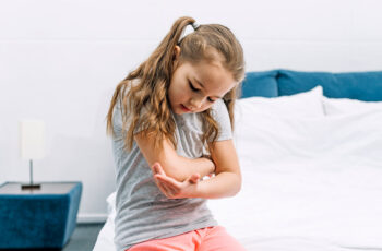 дитина сидить вдома на ліжку та намагається роздивитися лікоть