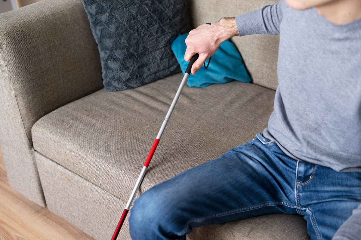 сліпий чоловік спирається на спеціальну палицю для людей із вадами зору